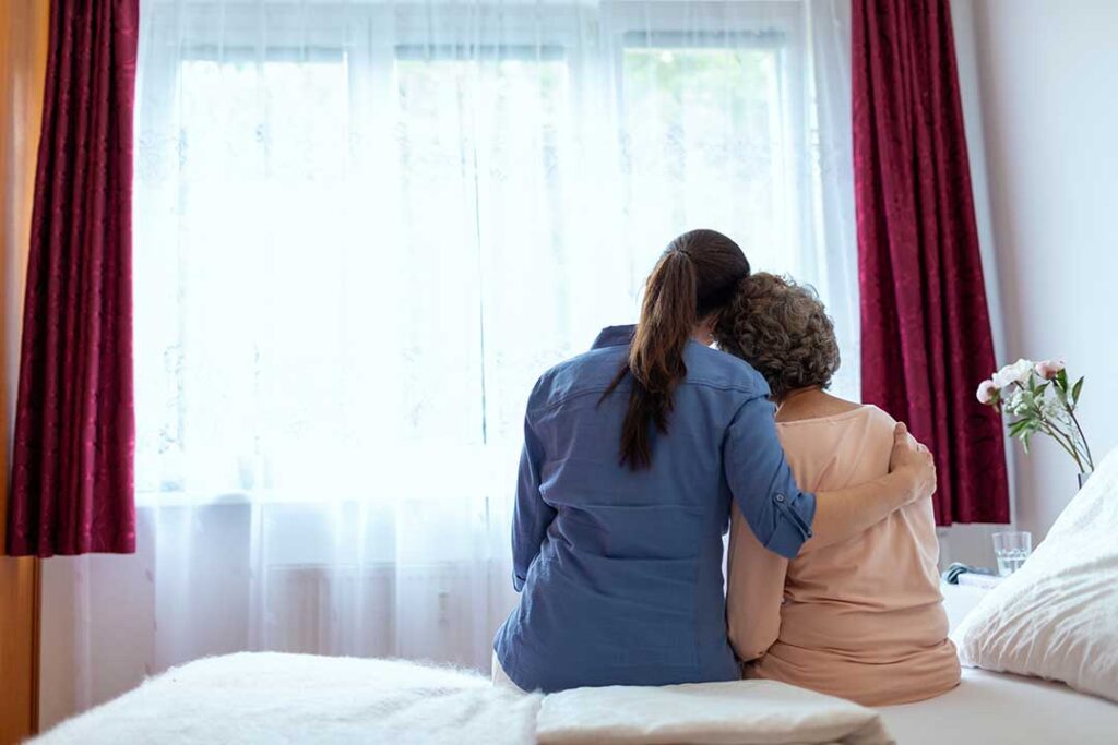 Older LGBTQ+ adults and a caregiver having a respectful conversation in a bright assisted living common room.