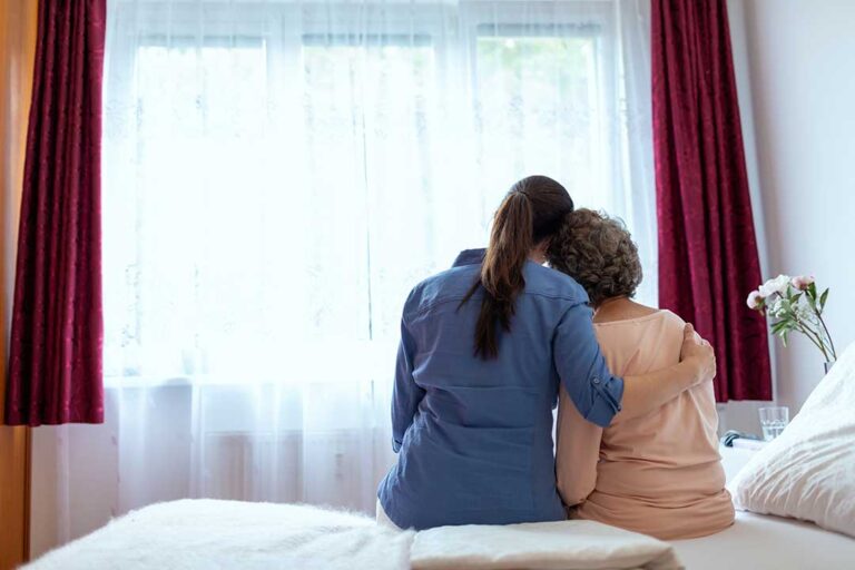 Older LGBTQ+ adults and a caregiver having a respectful conversation in a bright assisted living common room.
